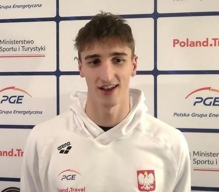 Ksawery Masiuk podczas pływania stylem grzbietowym, z kroplami wody na twarzy, ukazujący siłę i determinację.