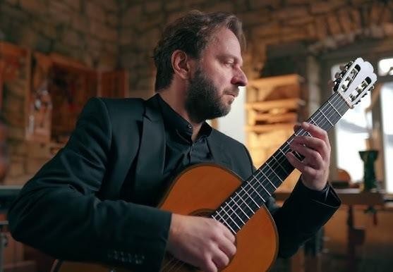 Zbliżenie na gryf gitary klasycznej z dłonią grającą skomplikowany akord, podkreślające detale instrumentu i umiejętności muzyka.