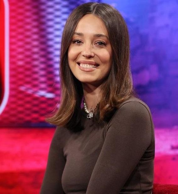 Izabella Krzan prowadząca program telewizyjny, uśmiechnięta i pełna energii, w tle widoczne studio telewizyjne.