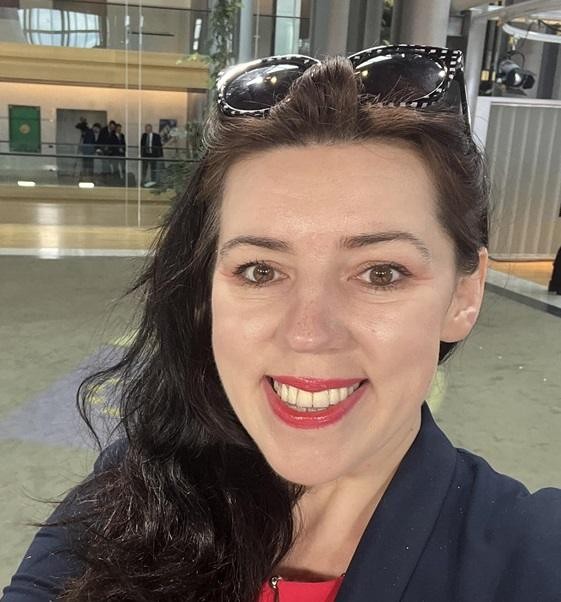 Dominika Ćosić podczas wystąpienia publicznego, z tłem nawiązującym do polityki europejskiej lub Bałkanów.
