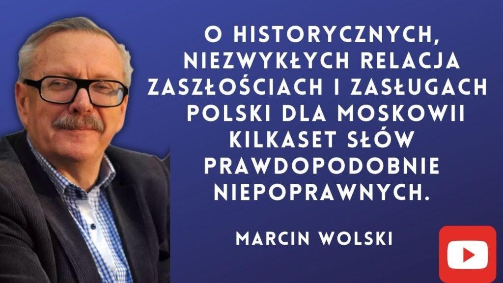Marcin Wolski, pisarz i satyryk, gestykulujący, w tle zamazane elementy symbolizujące literaturę i media.