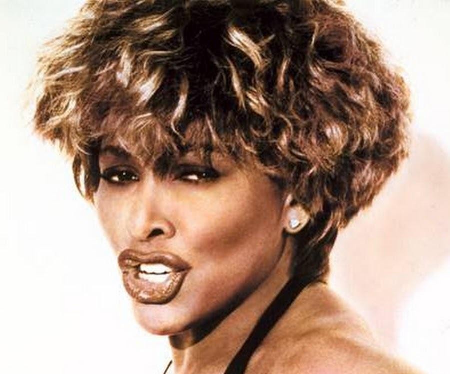 Tina Turner w starszym wieku, siedząca spokojnie w eleganckim wnętrzu, z łagodnym uśmiechem i widokiem na jezioro.