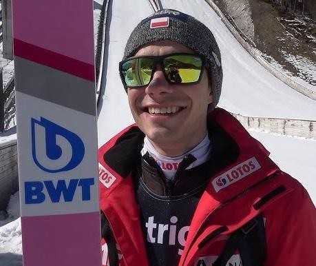 Jakub Wolny celebrujący sukces na skoczni narciarskiej, w stroju sportowym, z widocznym fragmentem publiczności w tle.